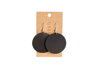 Display presents chic, round black leather earrings hanging on a branded retail card.
