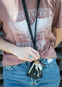 A woman wearing a graphic tee and jeans holds keys attached to a leather lanyard wallet.
