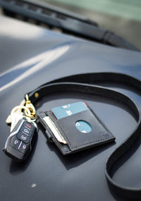 Car keys, a leather lanyard wallet holding cash and credit cards, sit on a car hood.
