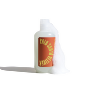 Palo Santo Vetiver body wash bottle sits amidst fluffy white lather against a bright white backdrop.
