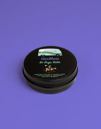 Close-up shows a tin of VanMan's No Bugs Balm, featuring a whimsical design of a VW van and a frog riding a cow, highlighting the natural ingredients like citronella and eucalyptus oil for effective insect repellent.
