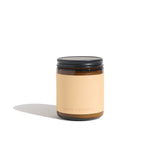 Studio shot presents a Sumac Campfire scented candle, featuring an amber glass jar, minimalist label, and black lid.

