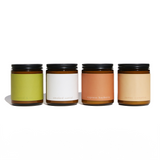 Four scented candles featuring sandalwood and campfire aromas sit in a row.
