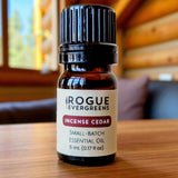 A bottle of Rogue Evergreens Incense Cedar essential oil sits on a wooden surface, showcasing its small-batch formulation and natural fragrance.
