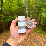 Someone holds Breathe Naturals Cedar Spice deodorant in an outdoor setting.
