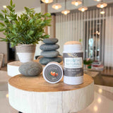 Breathe Naturals deodorant and Cedar Spice cream sit artfully on a wooden display amidst stacked stones and greenery.
