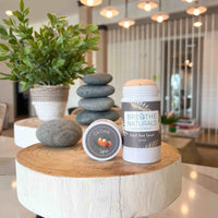 Breathe Naturals deodorant and Cedar Spice cream sit artfully on a wooden display amidst stacked stones and greenery.
