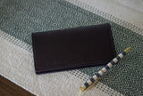 A black leather Urban Status wallet rests beside a stylish blue and white striped pen on a herringbone-patterned surface.
