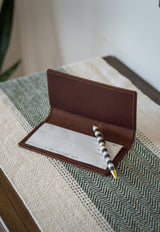 Striped pen rests on a blank check inside a brown leather checkbook holder.
