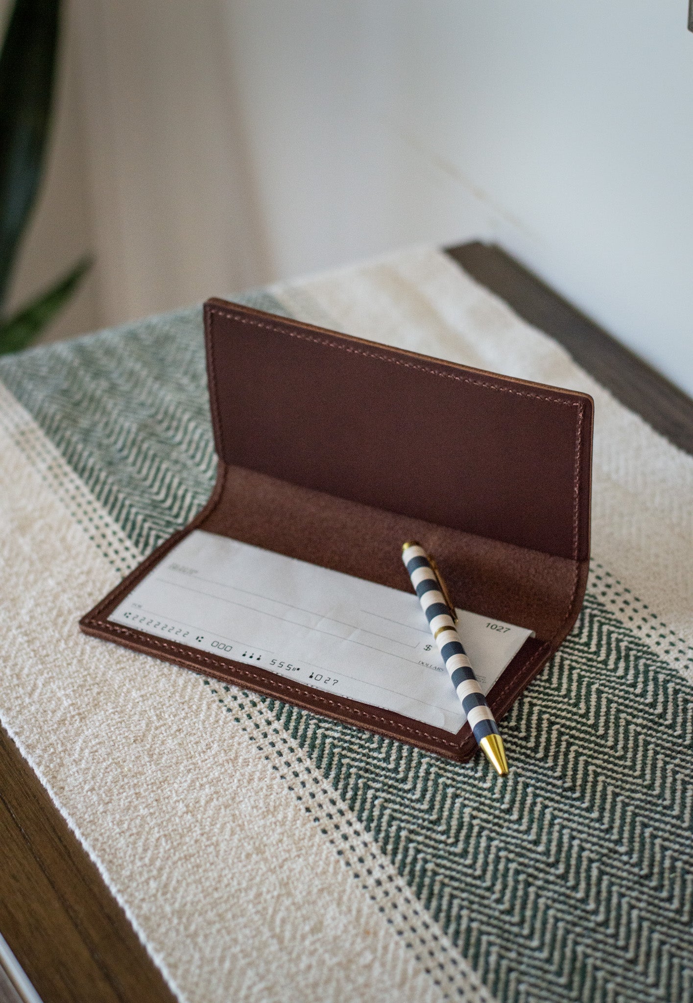 Striped pen rests on a blank check inside a brown leather checkbook holder.
