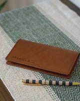 A brown leather wallet with "URBAN Southern" branding rests beside a striped pen on a textured cream and green surface.
