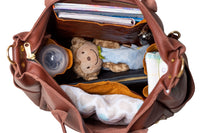Open brown leather diaper bag reveals baby bottle, plush monkey, diapers, muslin blanket, keys, and notebooks.
