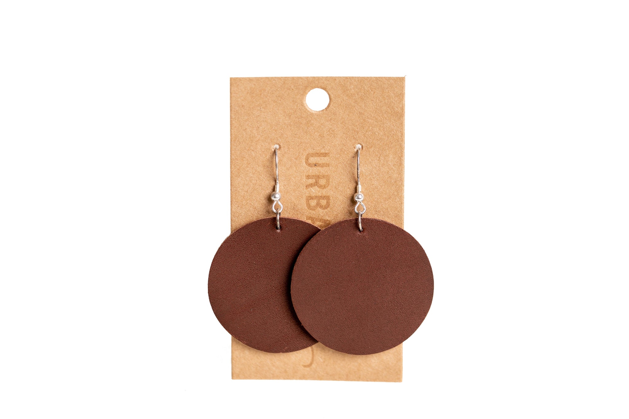Two brown, circular leather earrings dangle from silver hooks on a branded display card.
