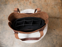 Open brown leather tote bag displays a black felt organizer with compartments.
