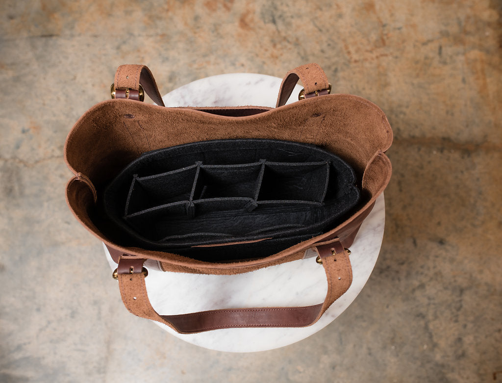 Open brown leather tote bag displays a black felt organizer with compartments.
