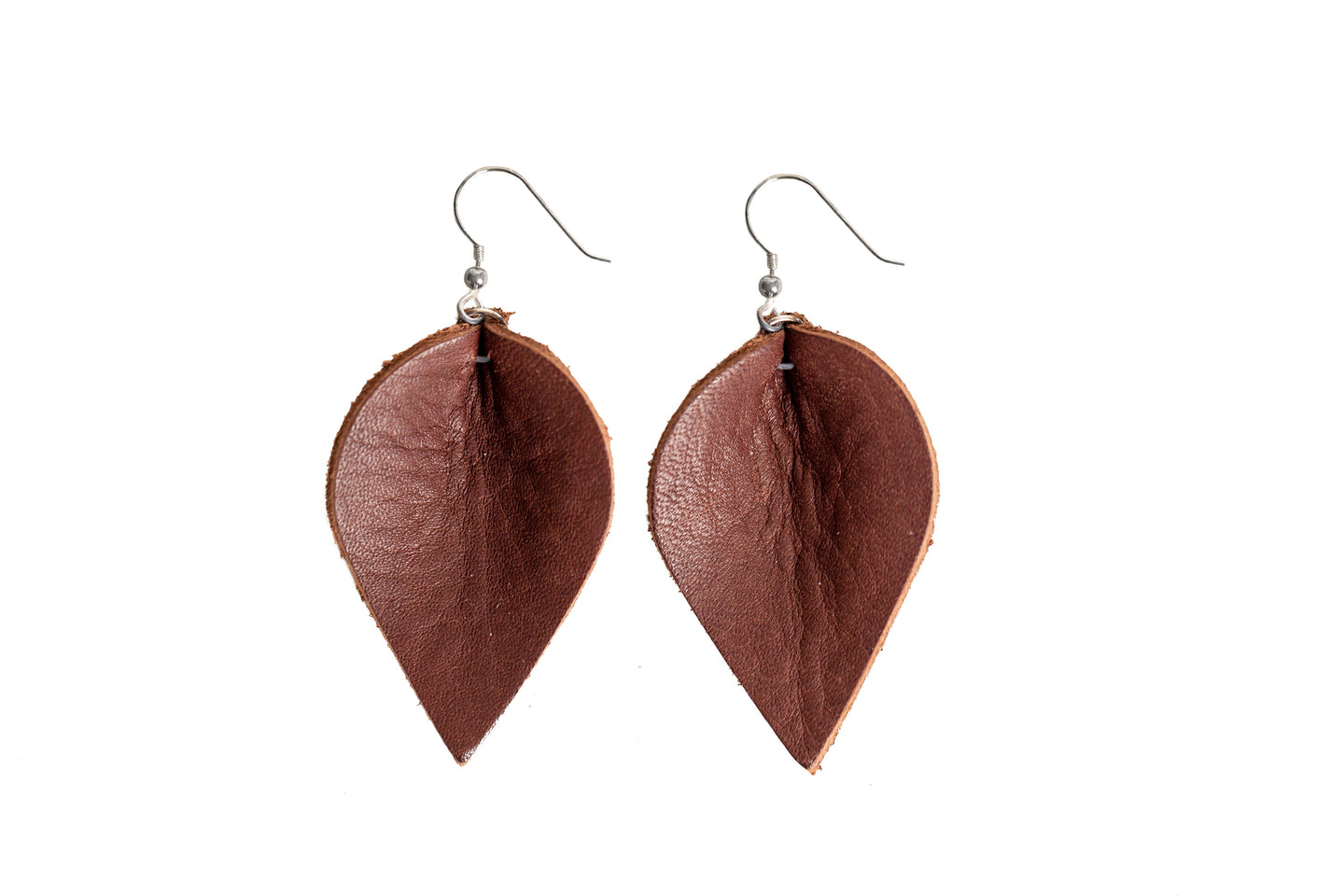 Two leaf-shaped brown leather earrings hang against a white background, showcasing their handmade design and silver hooks.
