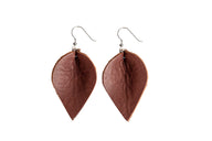 Two leaf-shaped brown leather earrings hang against a white background, showcasing their handmade design and silver hooks.
