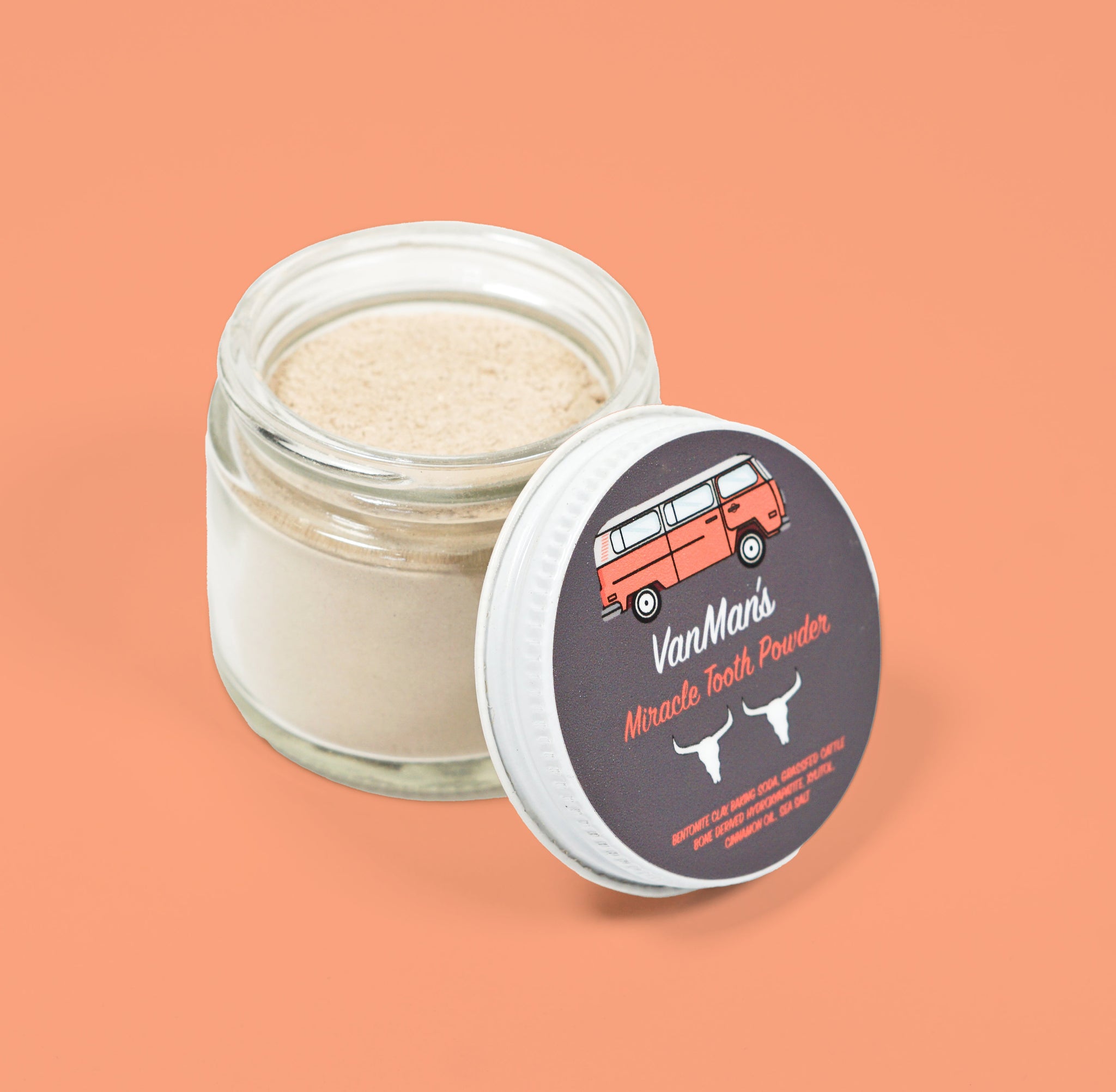 VanMan's Miracle Tooth Powder, a natural dental care product in a glass jar, sits with its lid featuring a vintage van illustration.
