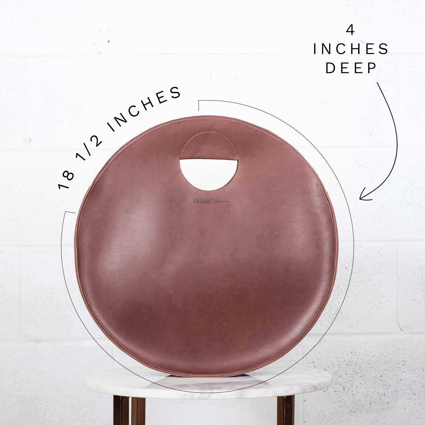 View showcases the dimensions of a stylish 18 1/2-inch round, 4-inch deep mauve leather tote bag with a unique circular handle.
