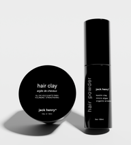 Displays Jack Henry hair clay and hair powder products, showcasing their minimalist black packaging.
