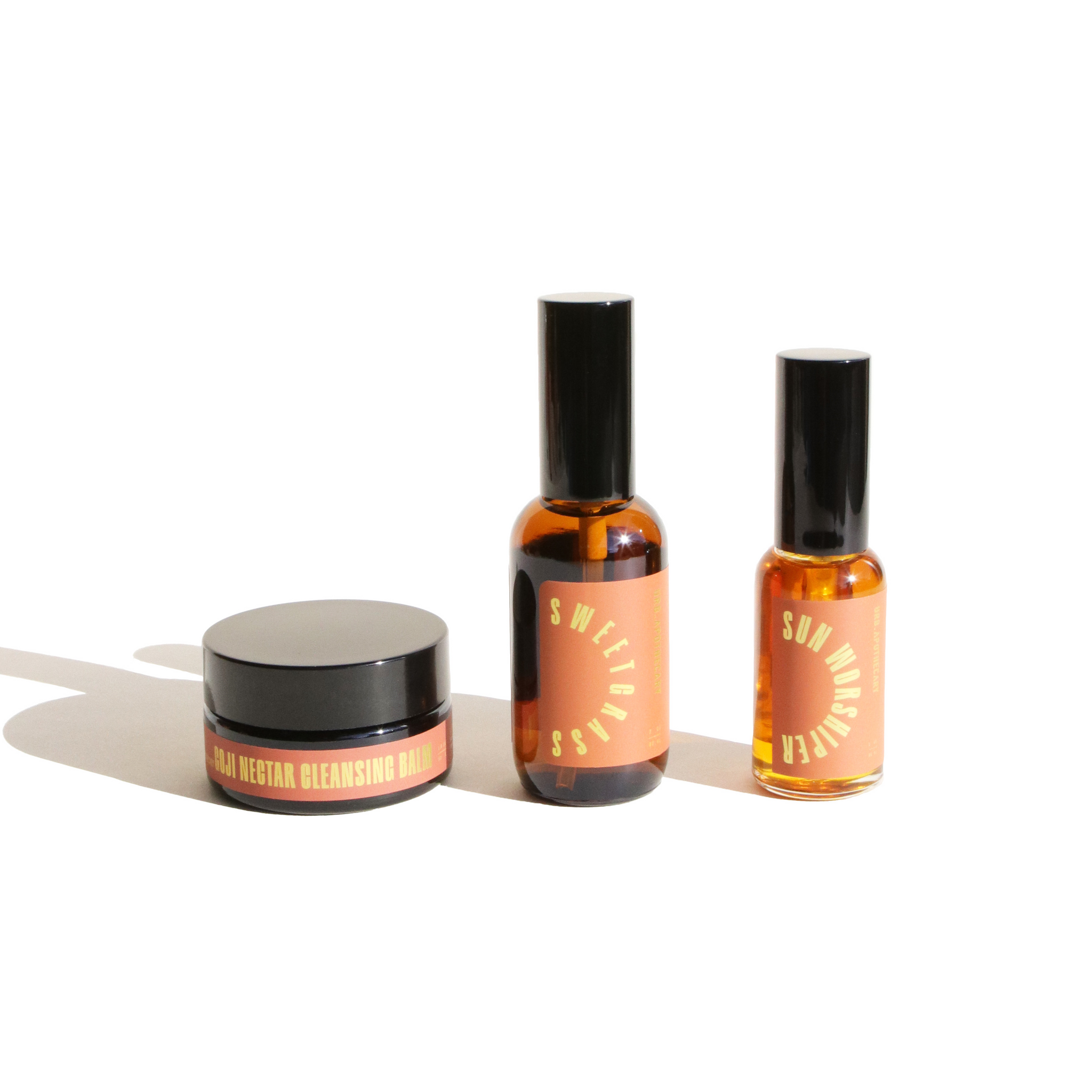 Three Ure Apothecary skincare products, including Goji Nectar Cleansing Balm, Sweetgrass serum, and Sun Worshiper oil, sit against a white background.
