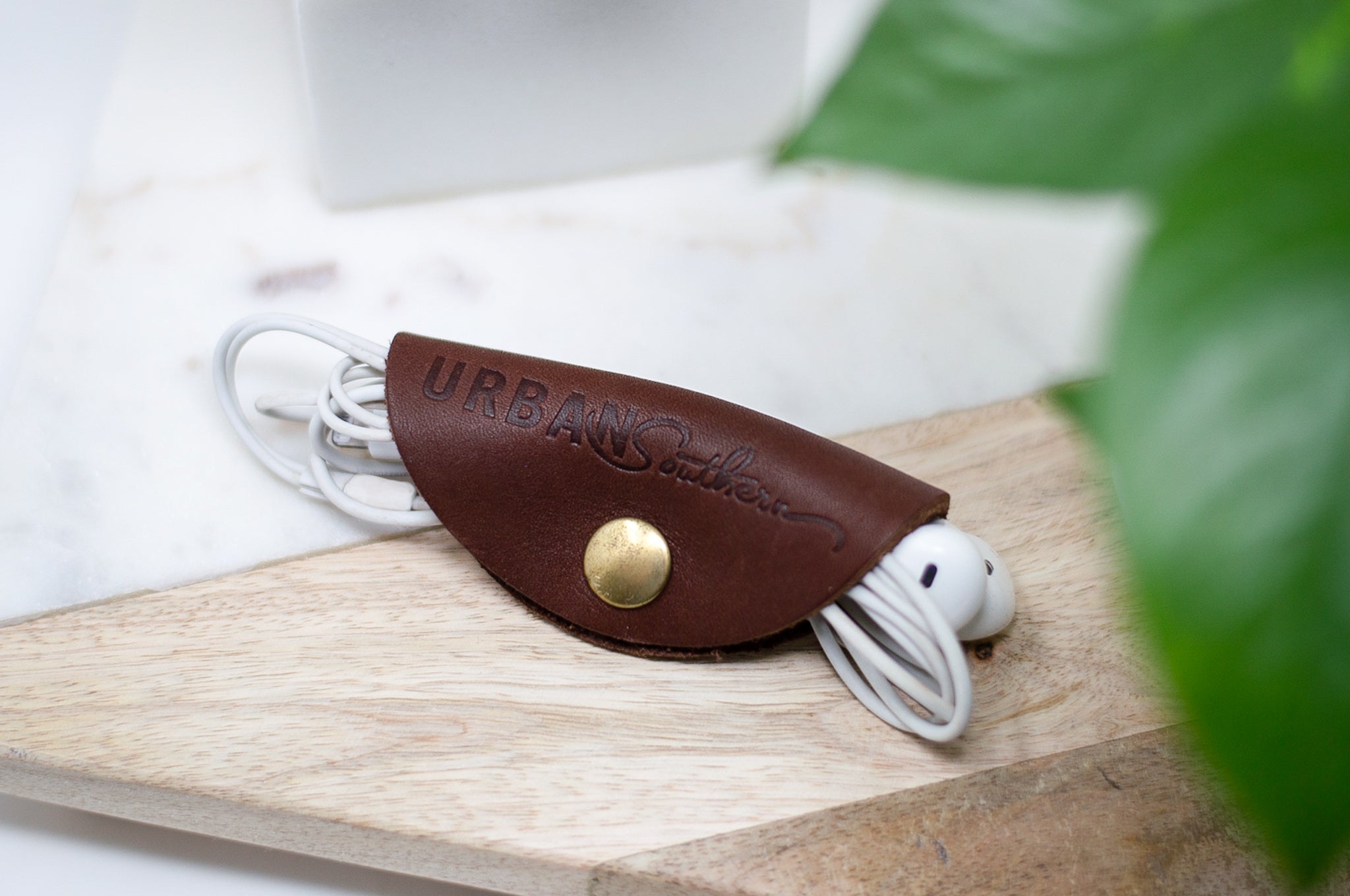 A leather earbud organizer secures white wired headphones on a wooden surface.
