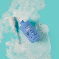 Dabble & Dollop Blueberry Gel bottle sits amidst bubbly foam on a bright teal surface.
