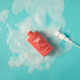 Strawberry gel body wash sits amidst bubbly foam on a bright blue surface.
