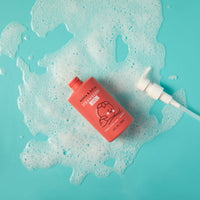 Strawberry gel body wash sits amidst bubbly foam on a bright blue surface.
