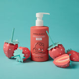 Display a bottle of Dabble & Dollop Strawberry Gel body wash and shampoo, surrounded by playful, handcrafted paper strawberries on a vibrant turquoise background.
