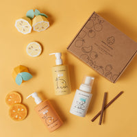 Dabble & Dollop presents a delightful collection of citrus-scented kids' bath products, including lemon gel, tangerine gel, and vanilla whip, arranged with playful paper fruit cutouts and a charming gift box.
