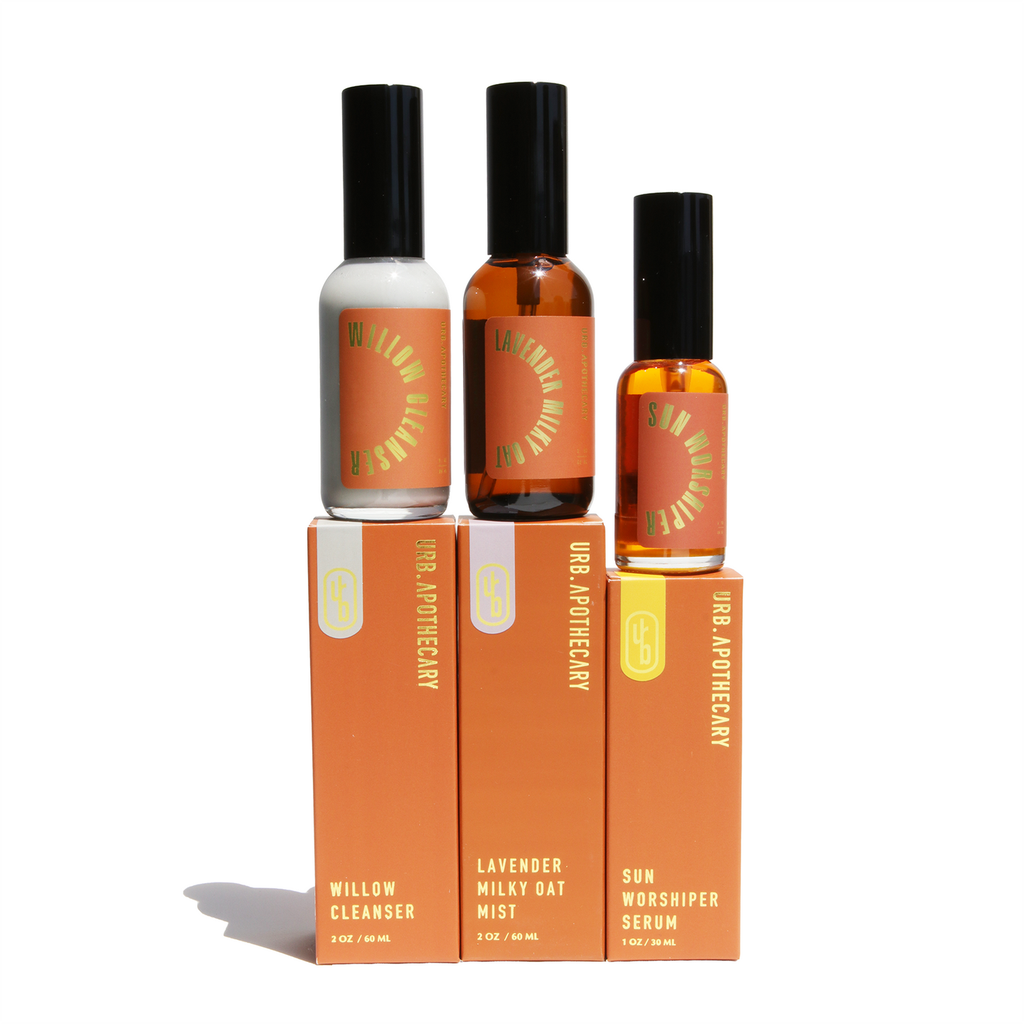 URB Apothecary presents its skincare line with Willow Cleanser, Lavender Milky Oat Mist, and Sun Worshiper Serum atop their labeled orange boxes.
