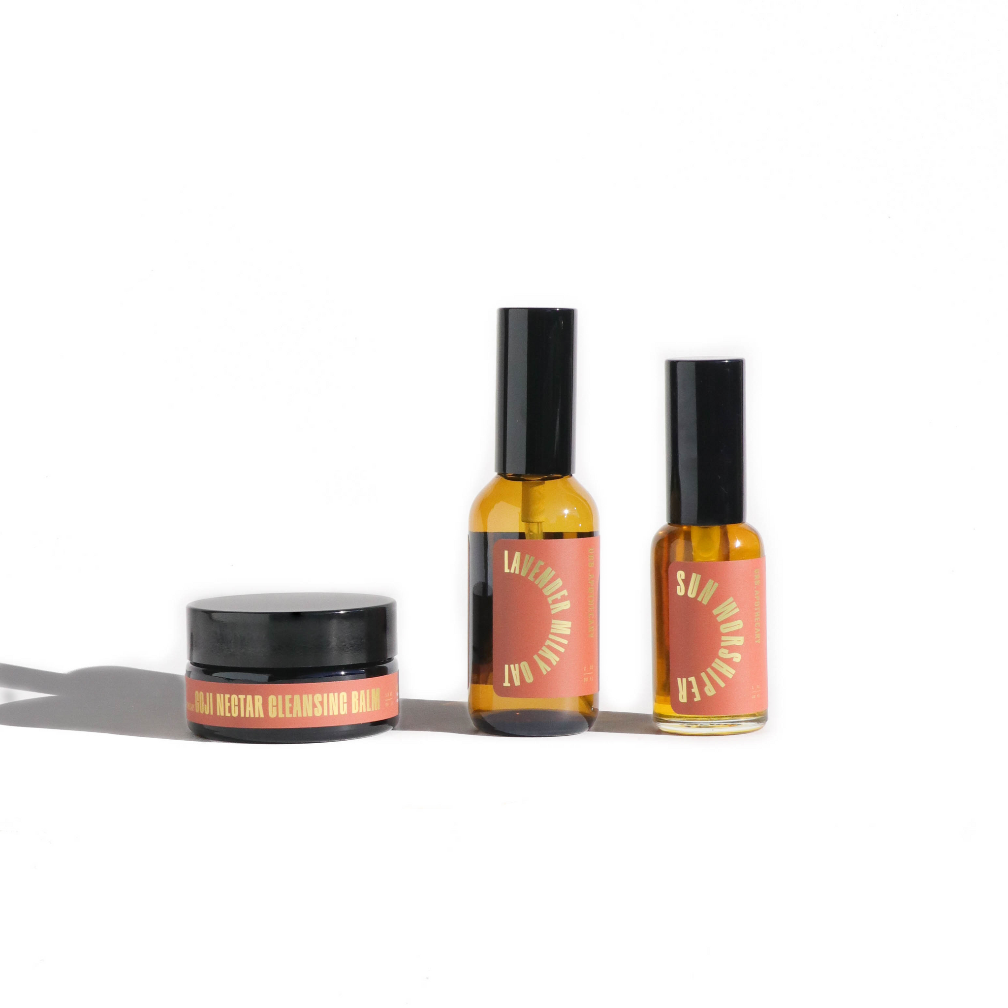URS Apothecary presents their Goji Nectar Cleansing Balm, Lavender Milky Oat facial toner, and Sun Worshiper facial oil on a clean, white background.
