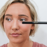 Woman holds Taylor Made Organics eyeliner pencil to her eye.
