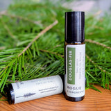 Two bottles of Rogue Evergreens Douglas-Fir essential oil roller lay amongst fresh evergreen boughs.
