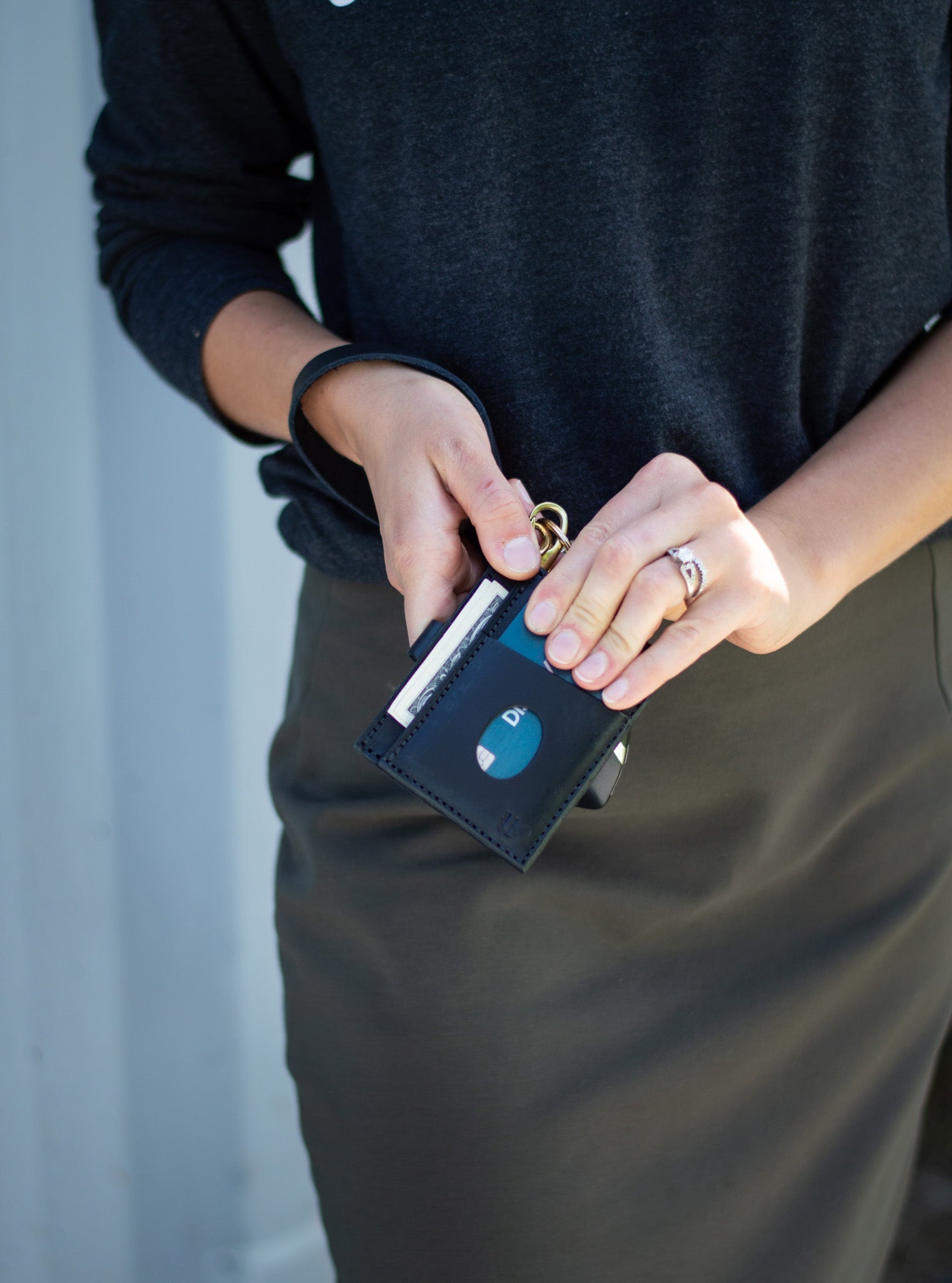 A woman takes a credit card from her black leather minimalist wallet attached to a key ring.
