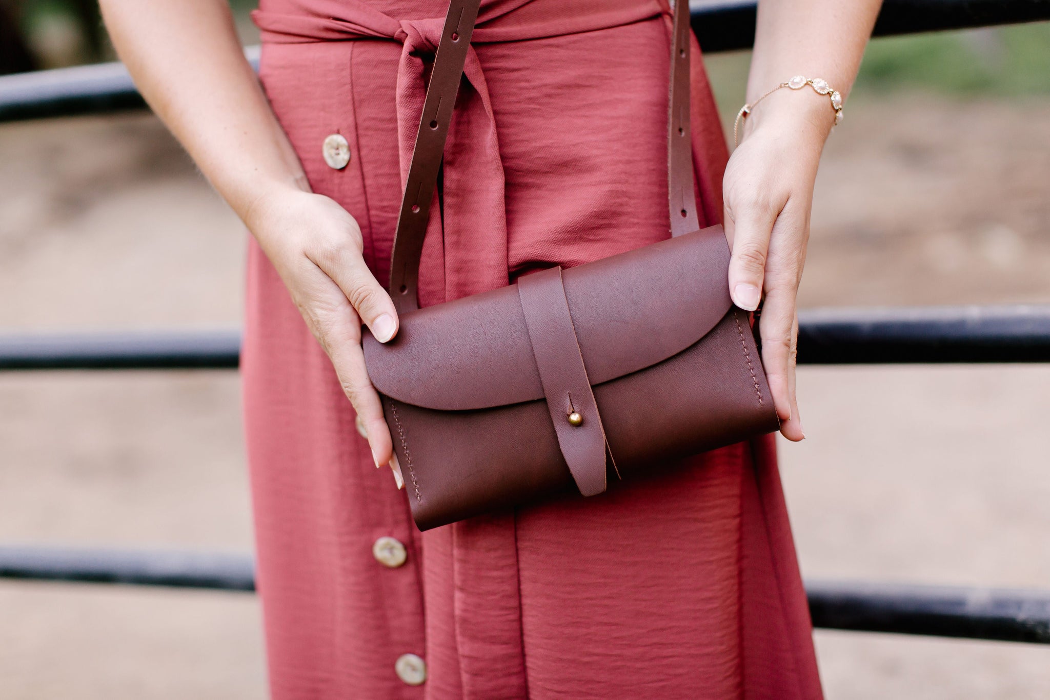 Woman showcases a handcrafted leather crossbody bag against a rusty rose dress.
