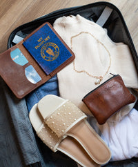 Traveler packs a suitcase with clothes, sandals, passport, and jewelry for a vacation.

