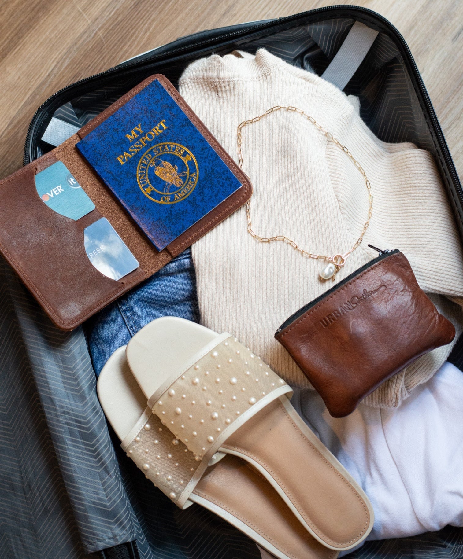 Traveler packs a suitcase with clothes, sandals, passport, and jewelry for a vacation.
