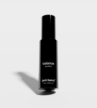 Jack Henry's "Balance" roll-on aromatherapy oil sits upright, casting a shadow on a bright white surface.

