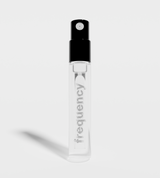 A clear glass Frequency perfume sample vial stands on a white surface.
