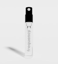 A clear glass Frequency perfume sample vial stands on a white surface.
