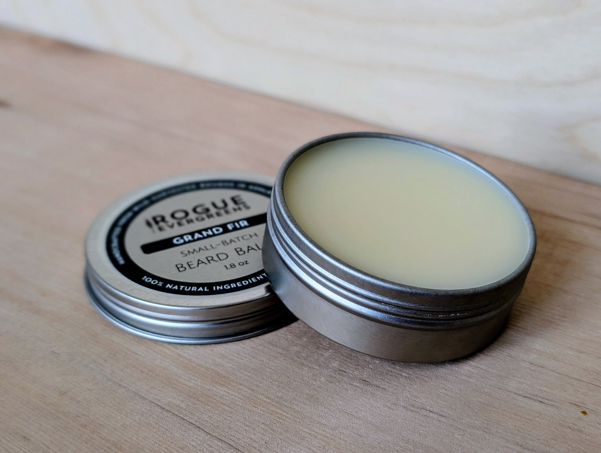 Two tins of Rogue Evergreens Grand Fir beard balm sit on a wooden surface.
