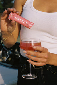 A woman prepares a refreshing GorgieGlow watermelon splash drink by adding the dietary supplement powder to a wine glass.

