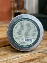 Close-up shows the label on a Rogue Evergreens beard balm tin, advertising natural ingredients like mango butter and fir essential oil to smooth, shape, moisturize, and protect beards.
