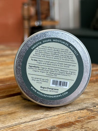 Close-up shows the label on a Rogue Evergreens beard balm tin, advertising natural ingredients like mango butter and fir essential oil to smooth, shape, moisturize, and protect beards.
