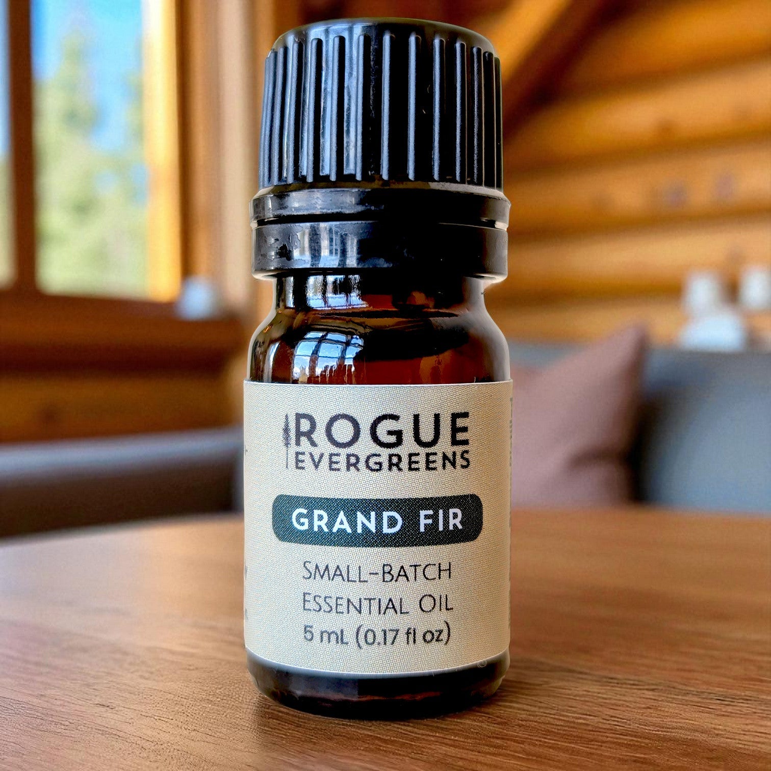Rogue Evergreens Grand Fir essential oil bottle sits on a wooden table indoors.
