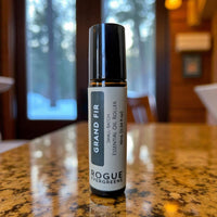 Rogue Evergreens Grand Fir essential oil roller sits on a reflective table near a window.
