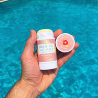 Person holds Breathe Naturals grapefruit and lemon natural deodorant above sparkling blue water.
