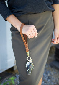 A person holds a leather keychain wristlet from Urban Southern with car keys and a remote.
